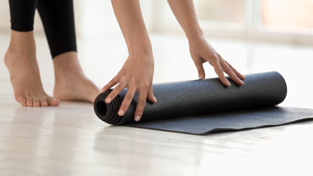 woman rolling out a black yoga mat to demonstrate stretches to alleviate lower back pain