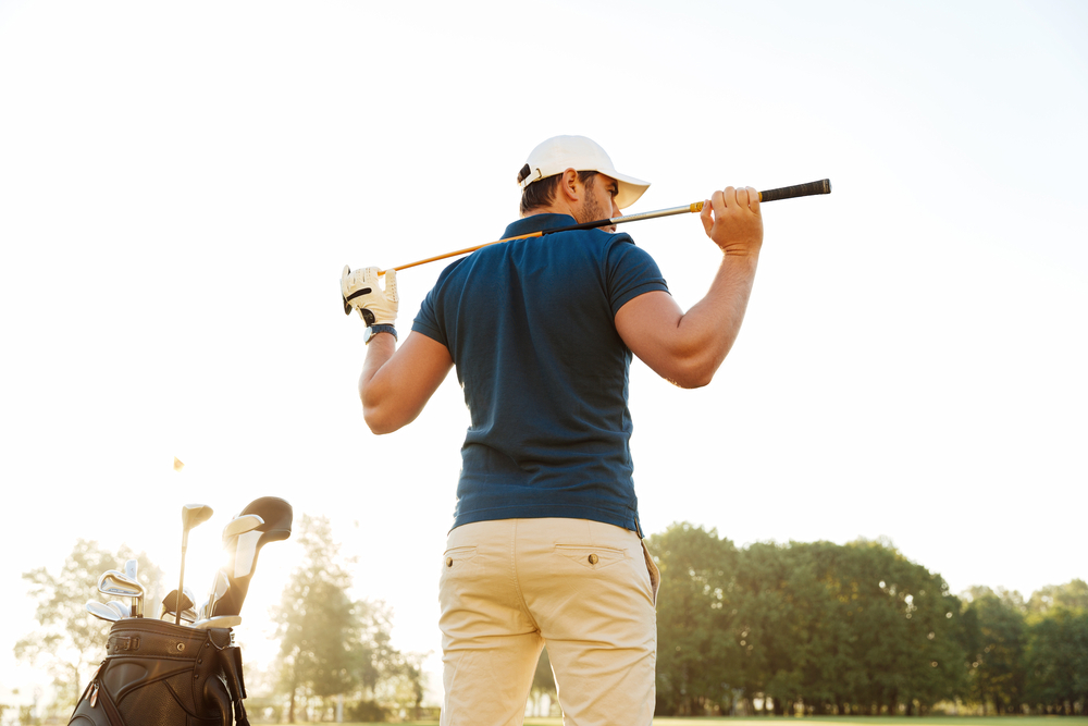 male golfer standing with his golf club resting behind his back in pain